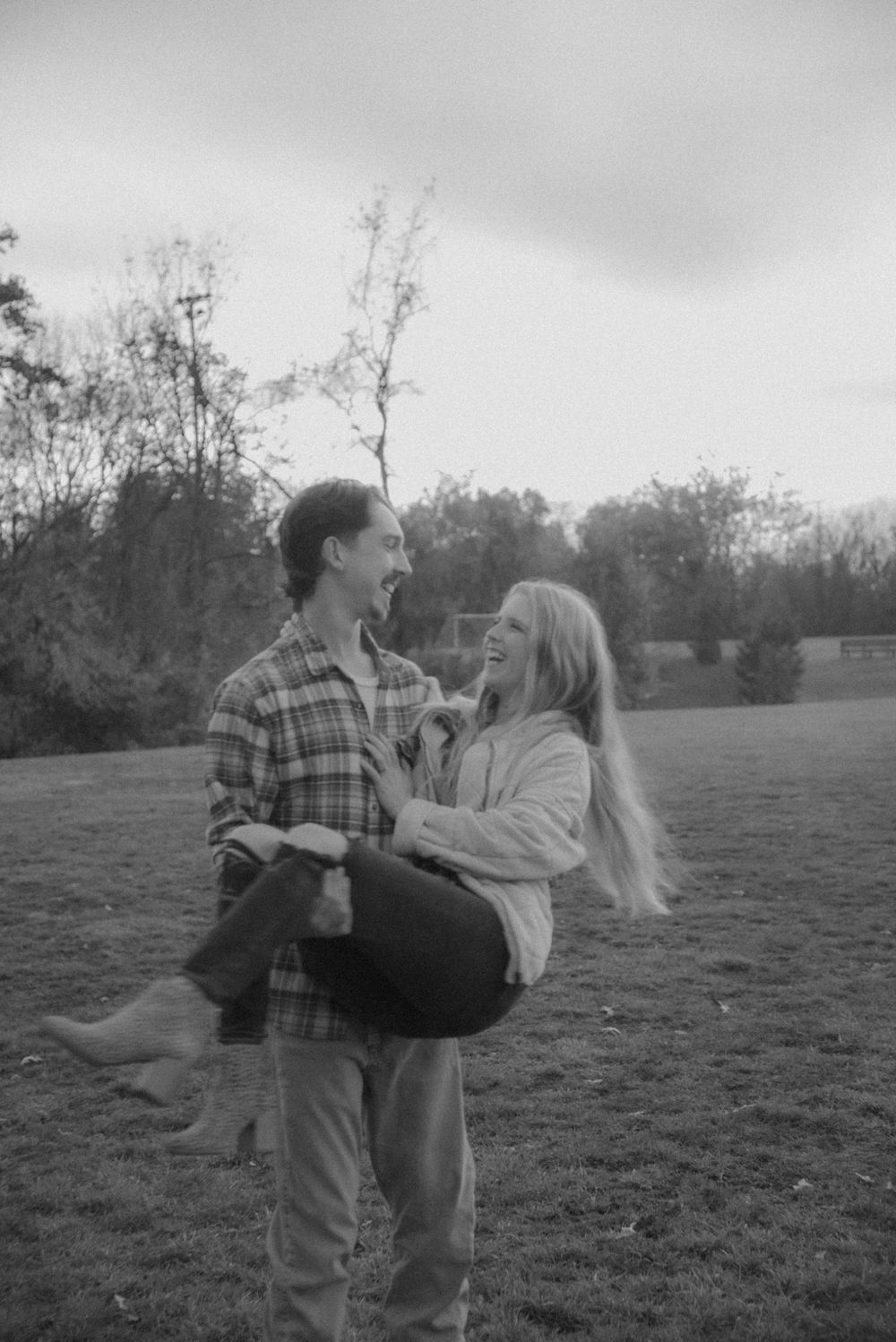 A playful black and white photo of a couple in a field.