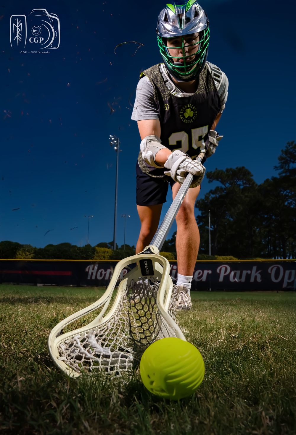 Lacrosse player in protective gear scooping up a bright yellow ball from grassy field during practice.