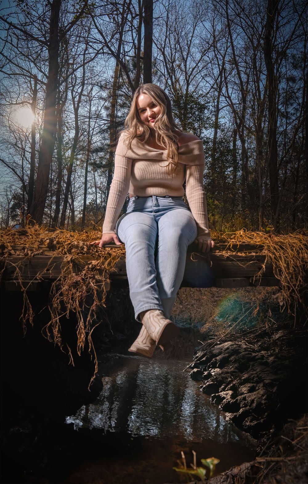 Person sits on fallen tree trunk over water during moody forest photoshoot at dusk.