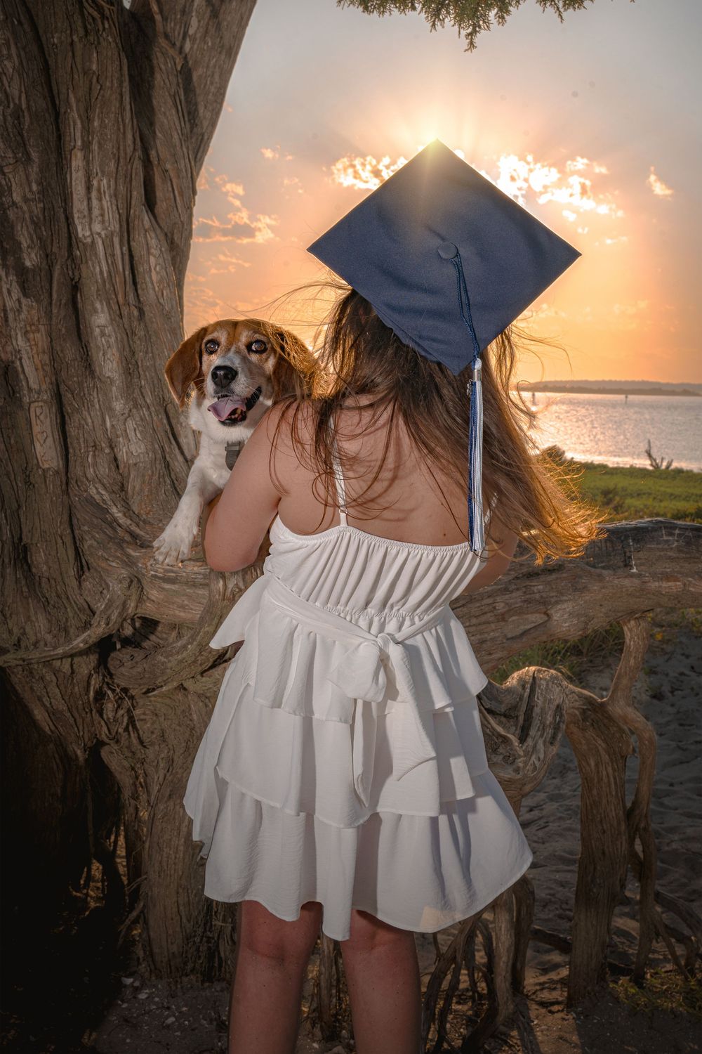 A series of graduation photos taken at sunset by the ocean featuring a white ruffle dress and graduation cap.