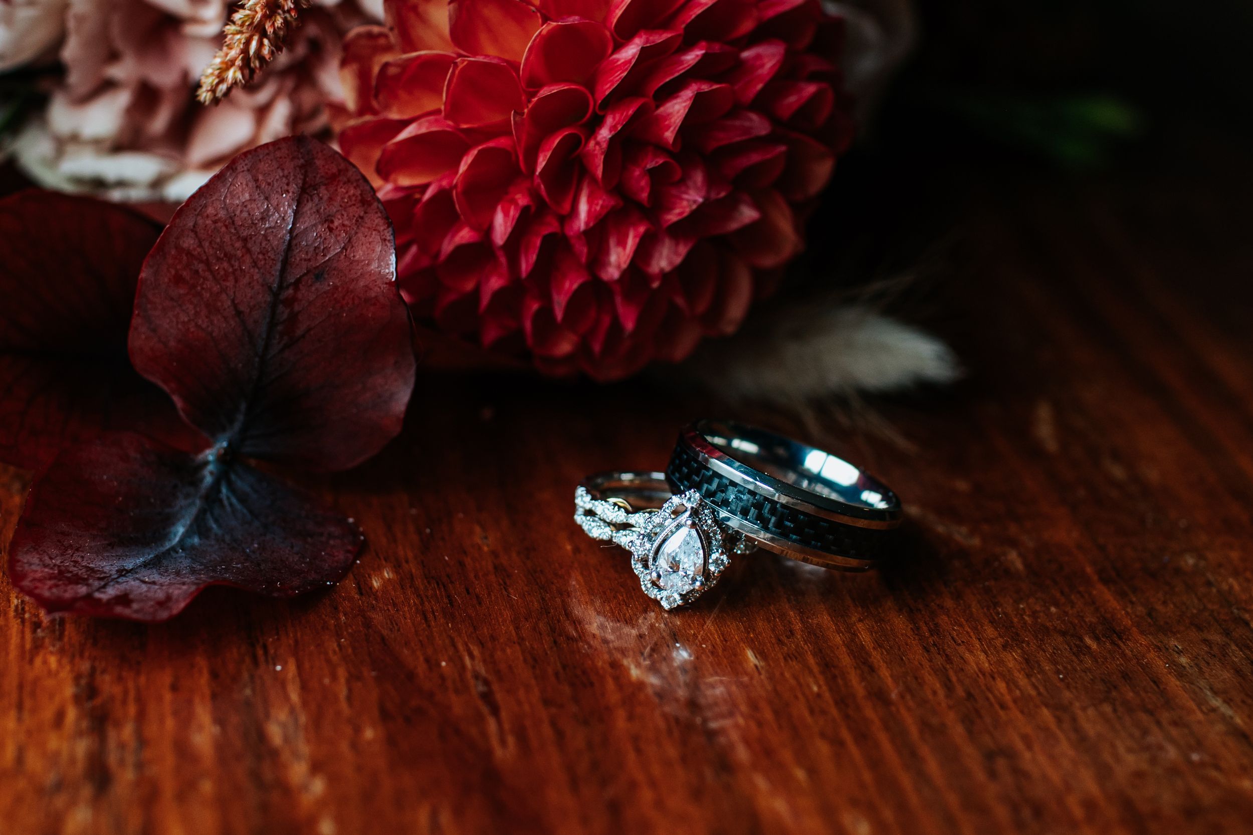 Deep red dahlia flowers arranged on a dark wooden surface create a moody and dramatic composition.