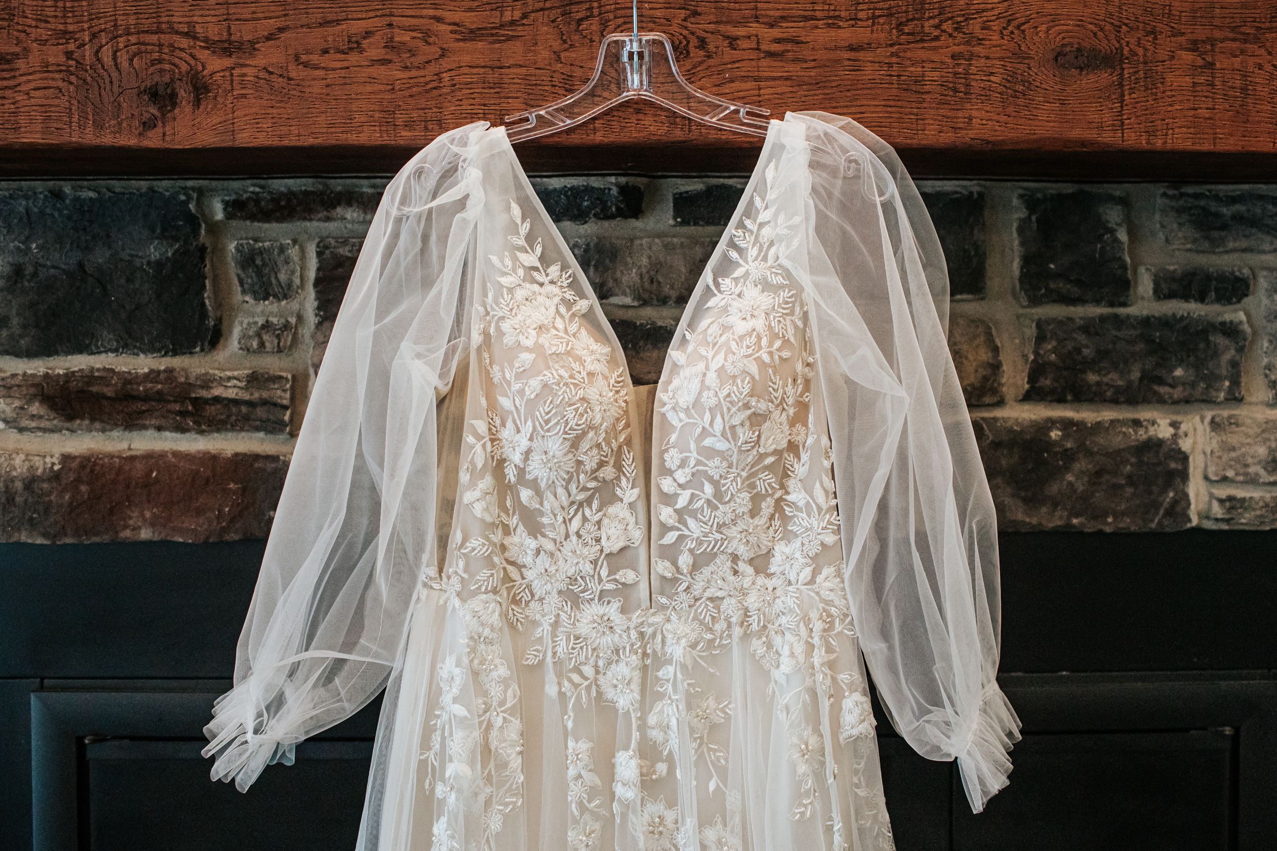 Elegant lace wedding dresses with delicate details hanging on display in a rustic stone wall setting.