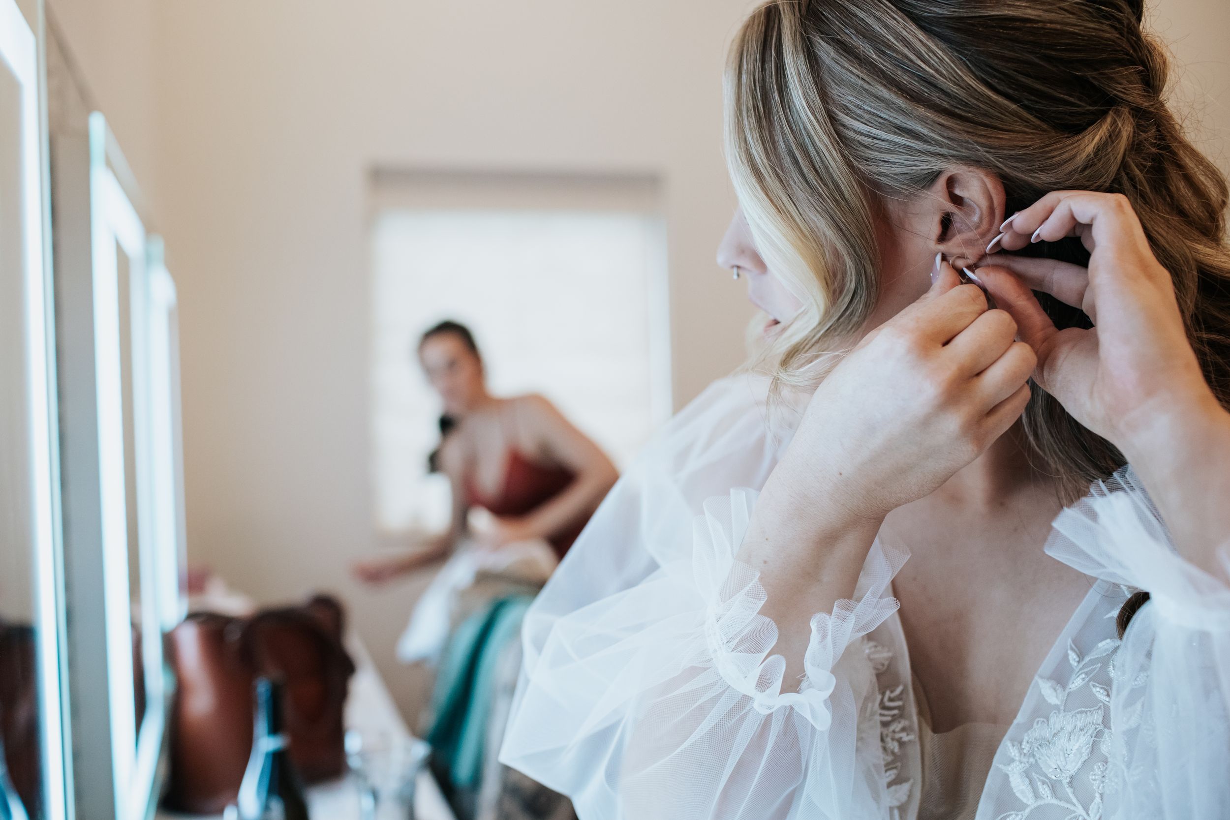 A group of people in formal attire getting ready for a wedding, with someone adjusting a white dress.