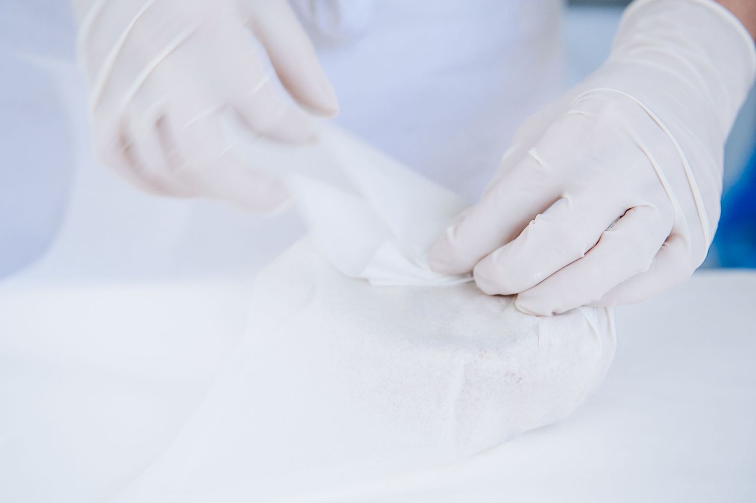 Close-up of hands wearing white medical gloves working on a light surface.