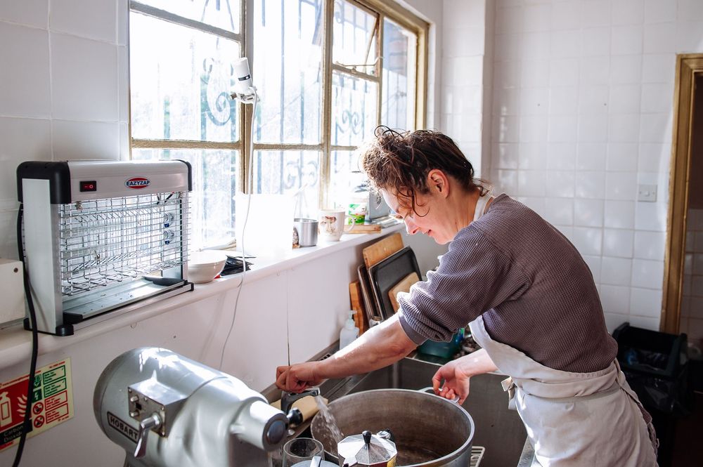 Person working in a bright commercial kitchen with white tiled walls and large windows.