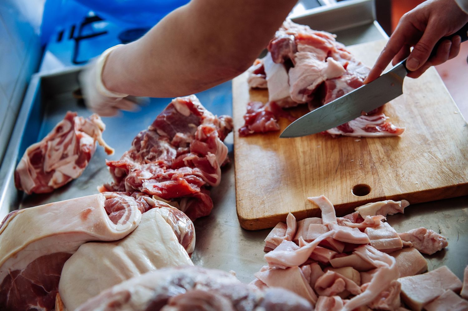 Raw meat being cut and prepared on a stainless steel work surface.