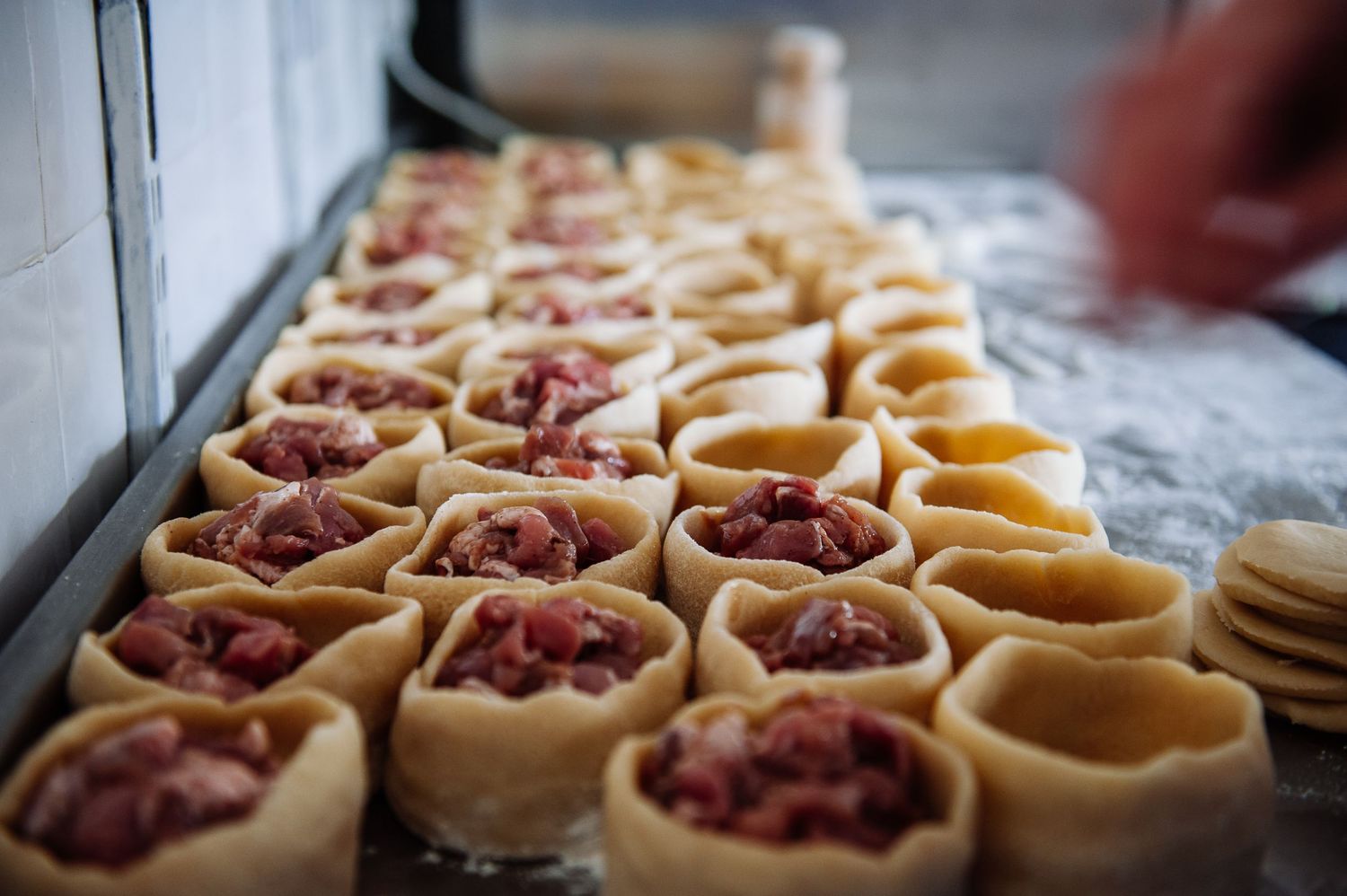 Small pastry shells filled with red meat mixture arranged in rows on a baking sheet.