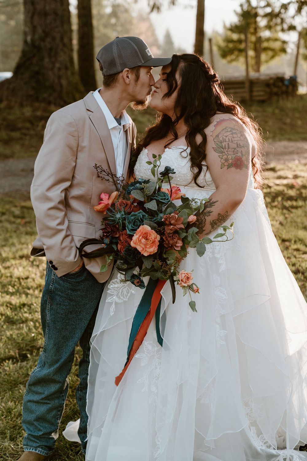 A bride and groom share a romantic nose-to-nose moment outdoors, she holds a vibrant coral and green bouquet with ribbon.
