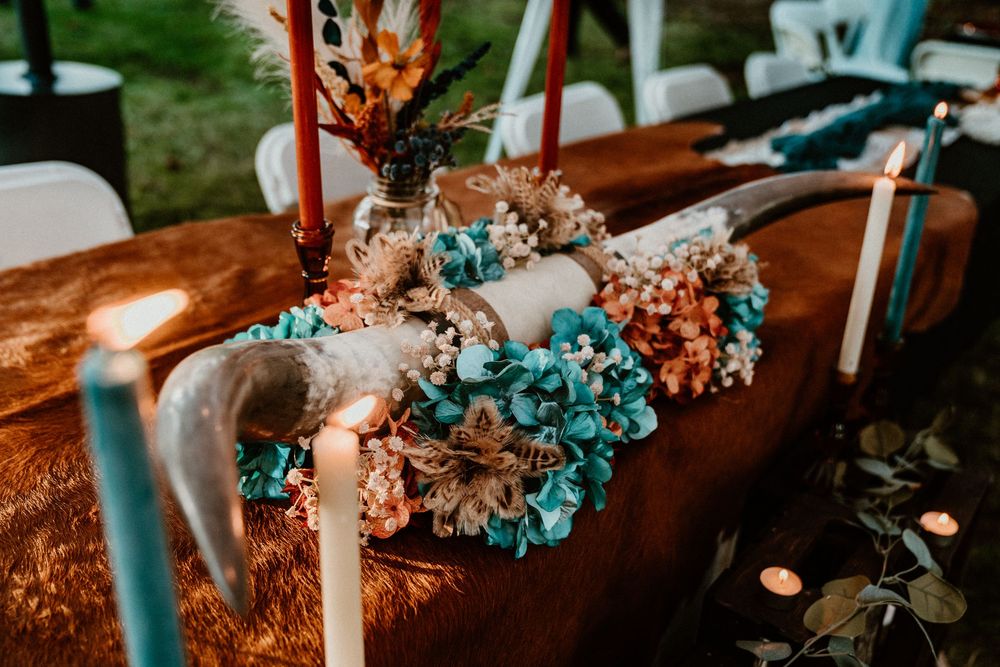 Rustic wedding table decor with teal hydrangeas, dried flowers, and candles on a wooden surface.