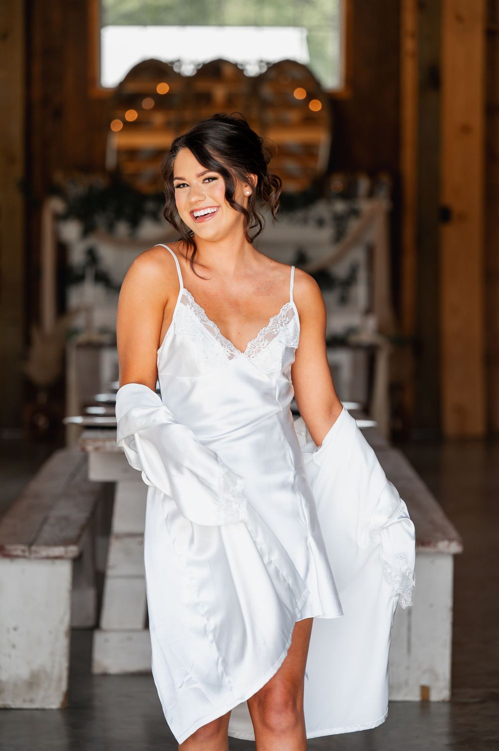 White silk bridal robe and dress in rustic barn setting with string lights.