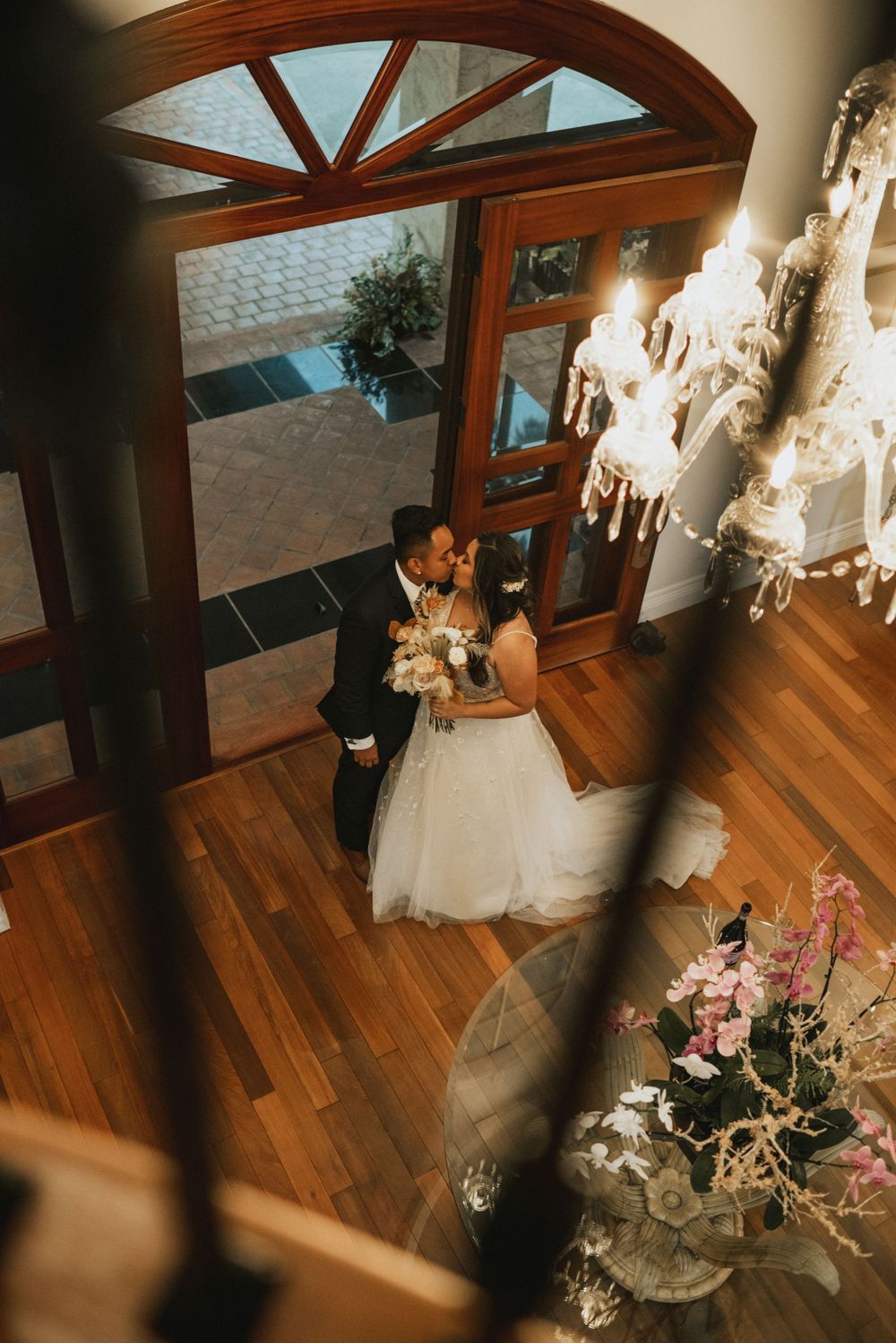 Wedding couple dances in an elegant venue with wooden floors and arched windows.