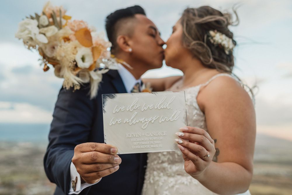 Couple shares intimate moment during outdoor wedding ceremony with decorative signage.