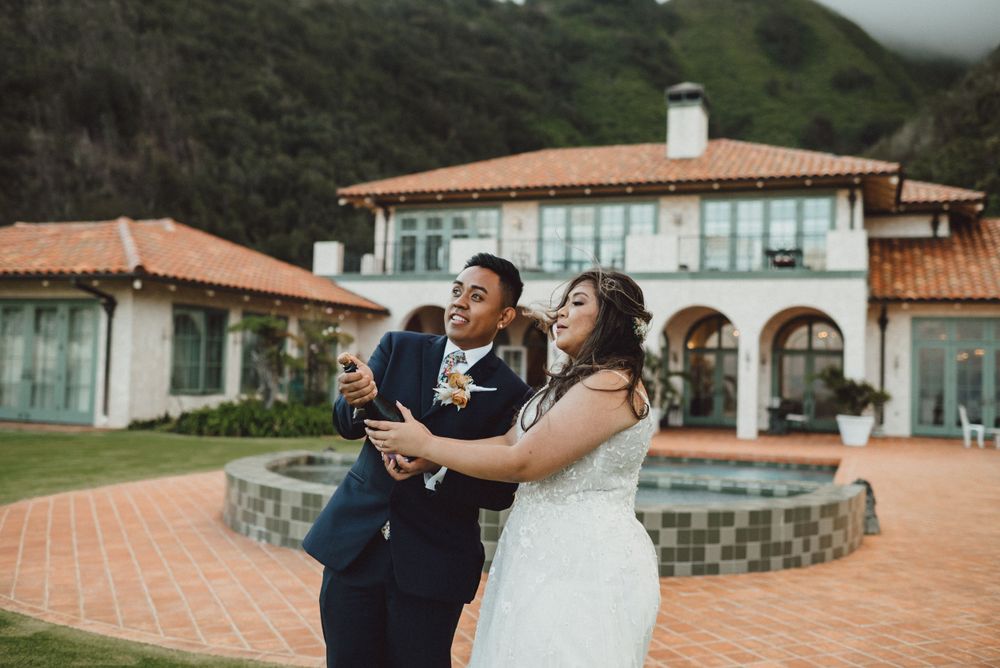 A couple in wedding attire shares a joyful moment by a pool at a Mediterranean villa.