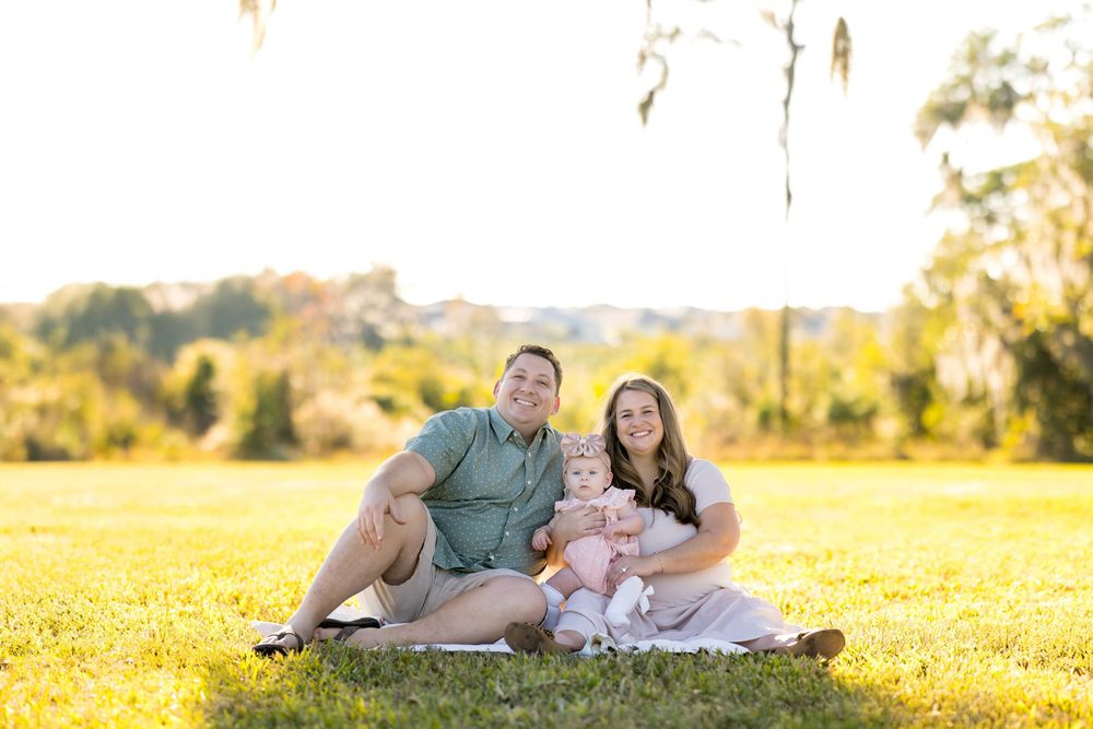 Family relaxing together on a blanket in a sunny meadow during golden hour.