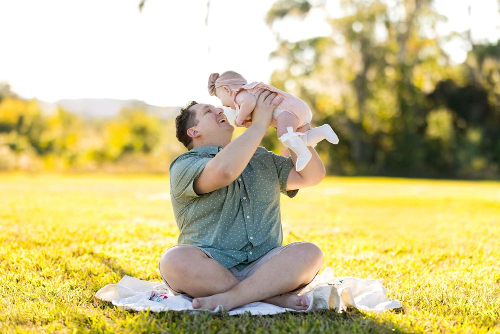 Person sitting cross-legged in a sunny meadow while drinking from a water bottle during golden hour.