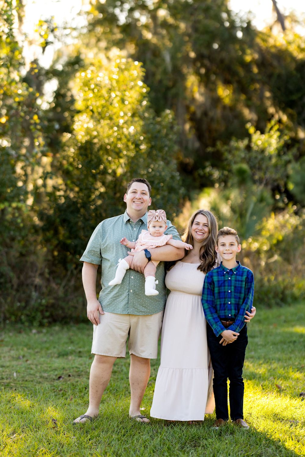 A family poses together outdoors in coordinated casual outfits during golden hour sunlight.