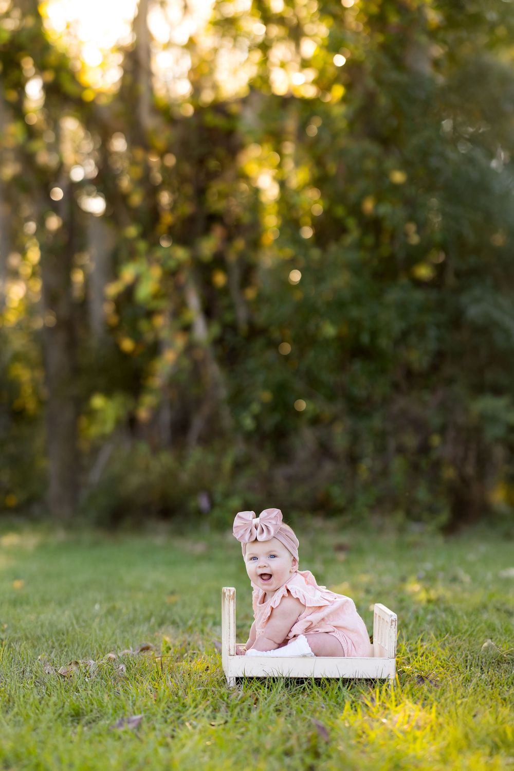 A small white bed sits in a grassy field at sunset with golden light filtering through trees in the background.