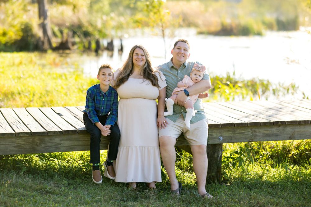 Family sits together on wooden dock during golden hour photo session in natural outdoor setting.