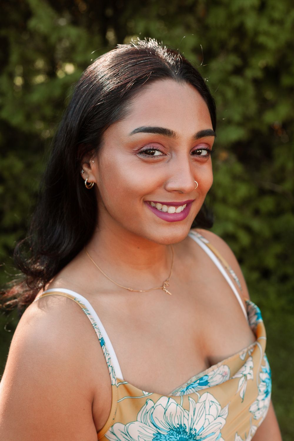 Young woman in a floral dress smiling brightly with a nose ring outdoors.