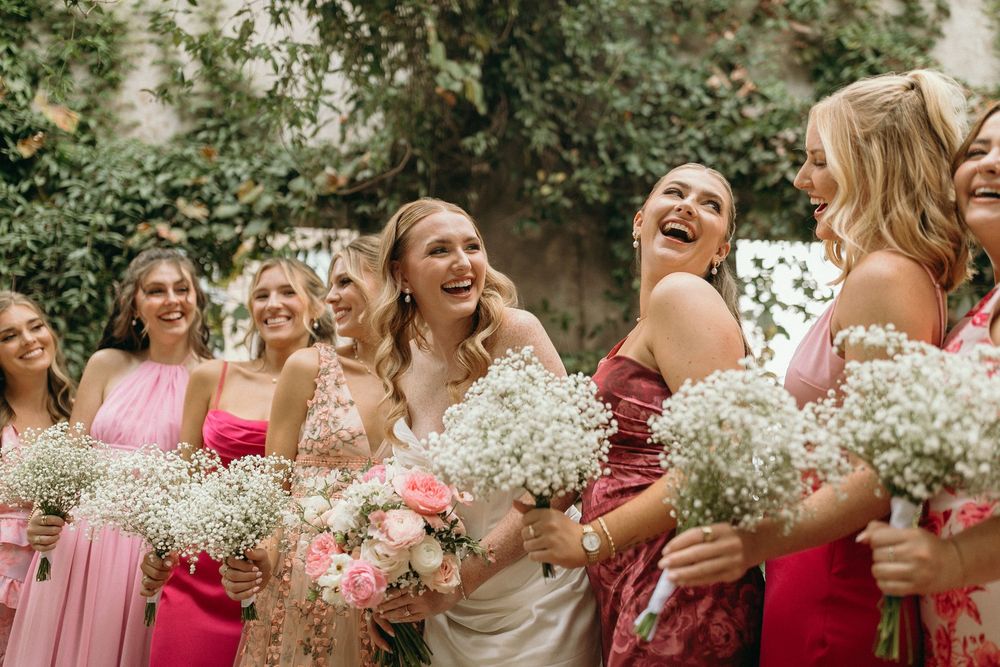 Bridesmaids in pink dresses laugh and hold white baby's breath bouquets during outdoor wedding celebration at Summerour Studio in Atlanta