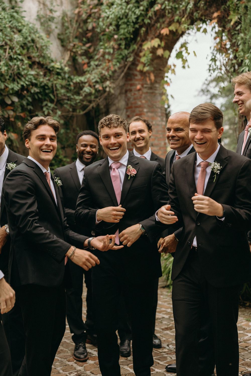 Groomsmen in black suits and pink ties share a candid laughing moment during a wedding photo session at Summerour Studio in Atlanta, Georgia