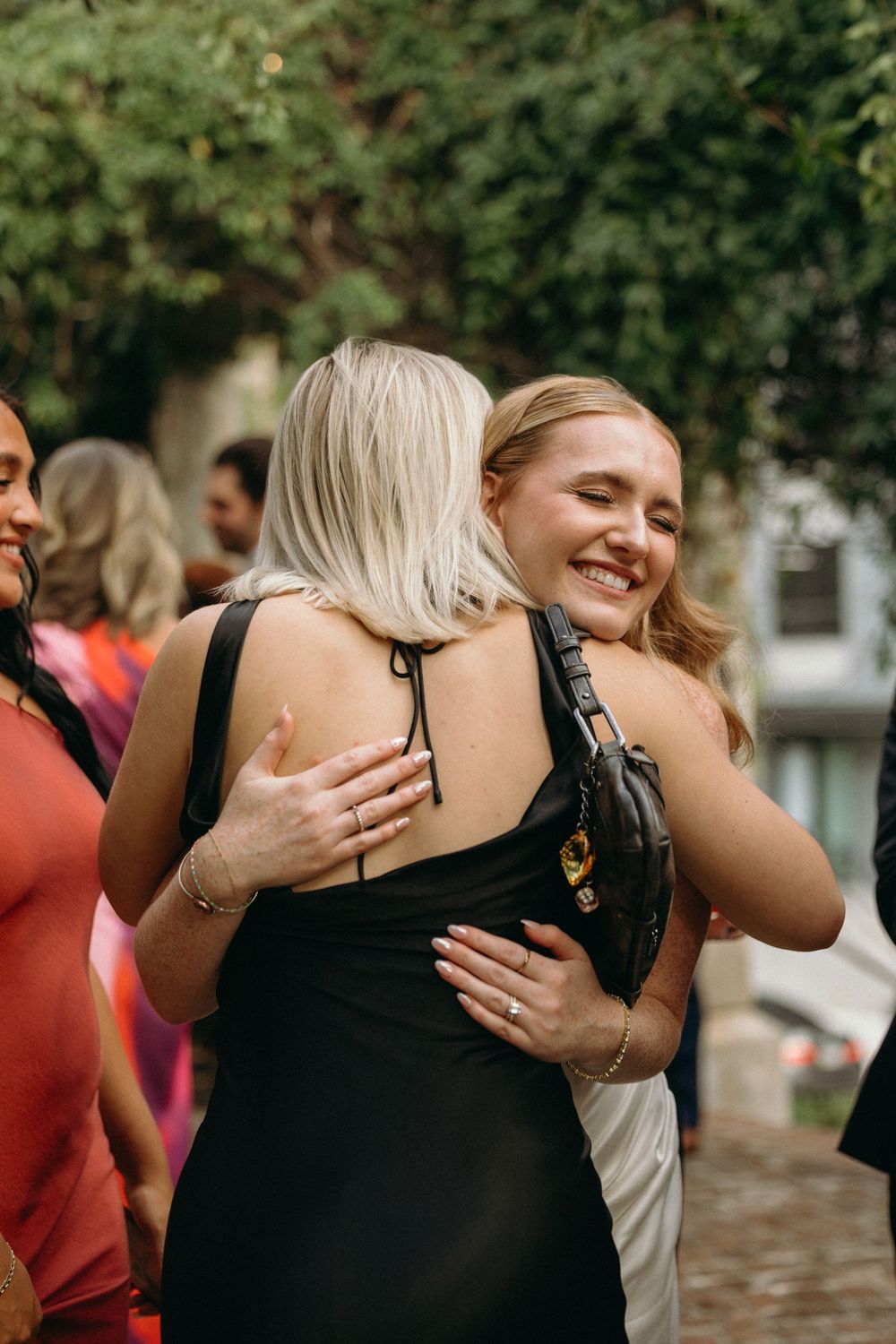 Two people sharing an emotional embrace outdoors during a gathering with others visible in the background at Summerour Studio in Georgia