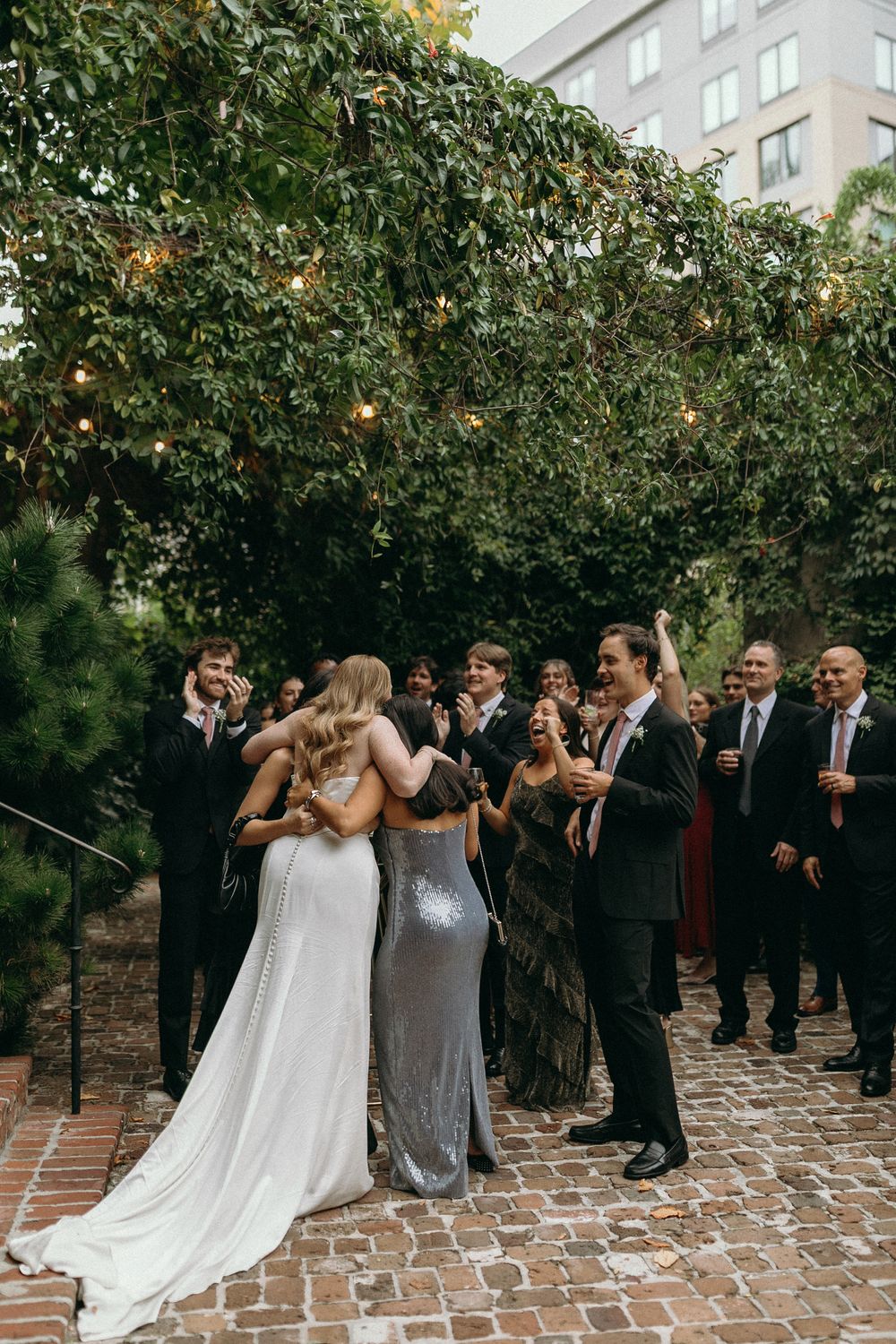 Wedding party in formal attire poses together on brick courtyard for candid group photos at Summerour Studio in Atlanta, Georgia