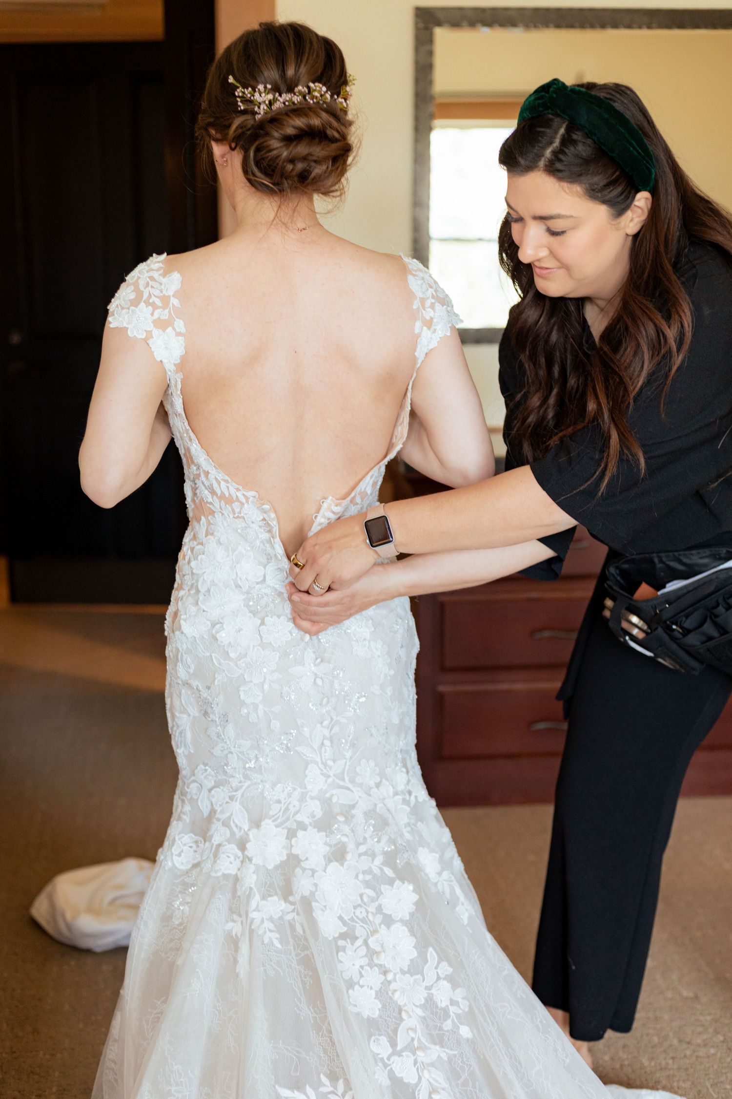 A sequence of photos showing someone helping to button up a white lace wedding dress with floral appliques.