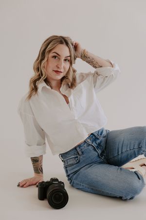 Casual photographer lounges on floor with camera in white shirt and blue jeans.