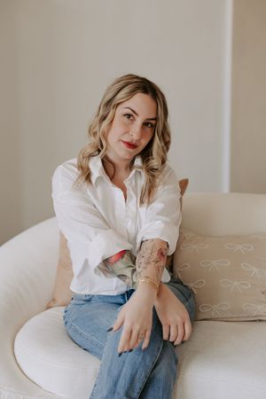 Casual portrait session on beige couch featuring white button-down shirt and denim.