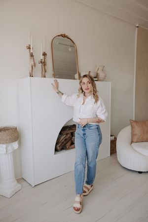 A lifestyle photoshoot featuring casual white top and jeans against a minimalist white interior backdrop.