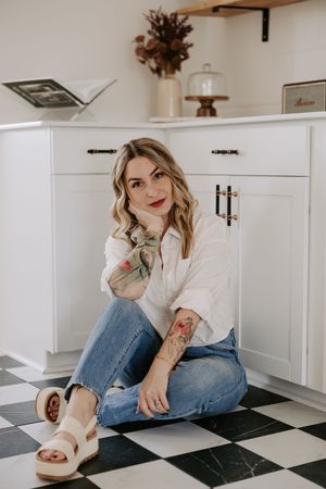 A casual lifestyle photoshoot on a black and white checkered floor in a bright white kitchen setting.