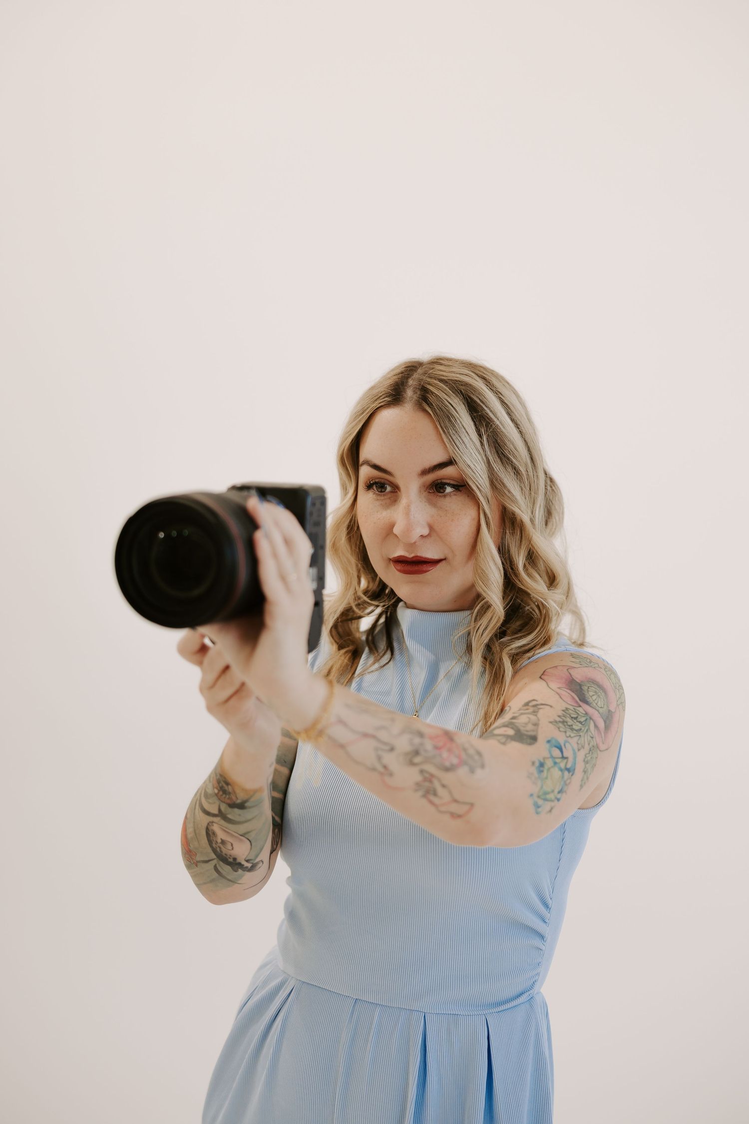 Photographer wearing blue dress demonstrates camera angles in studio photoshoot.