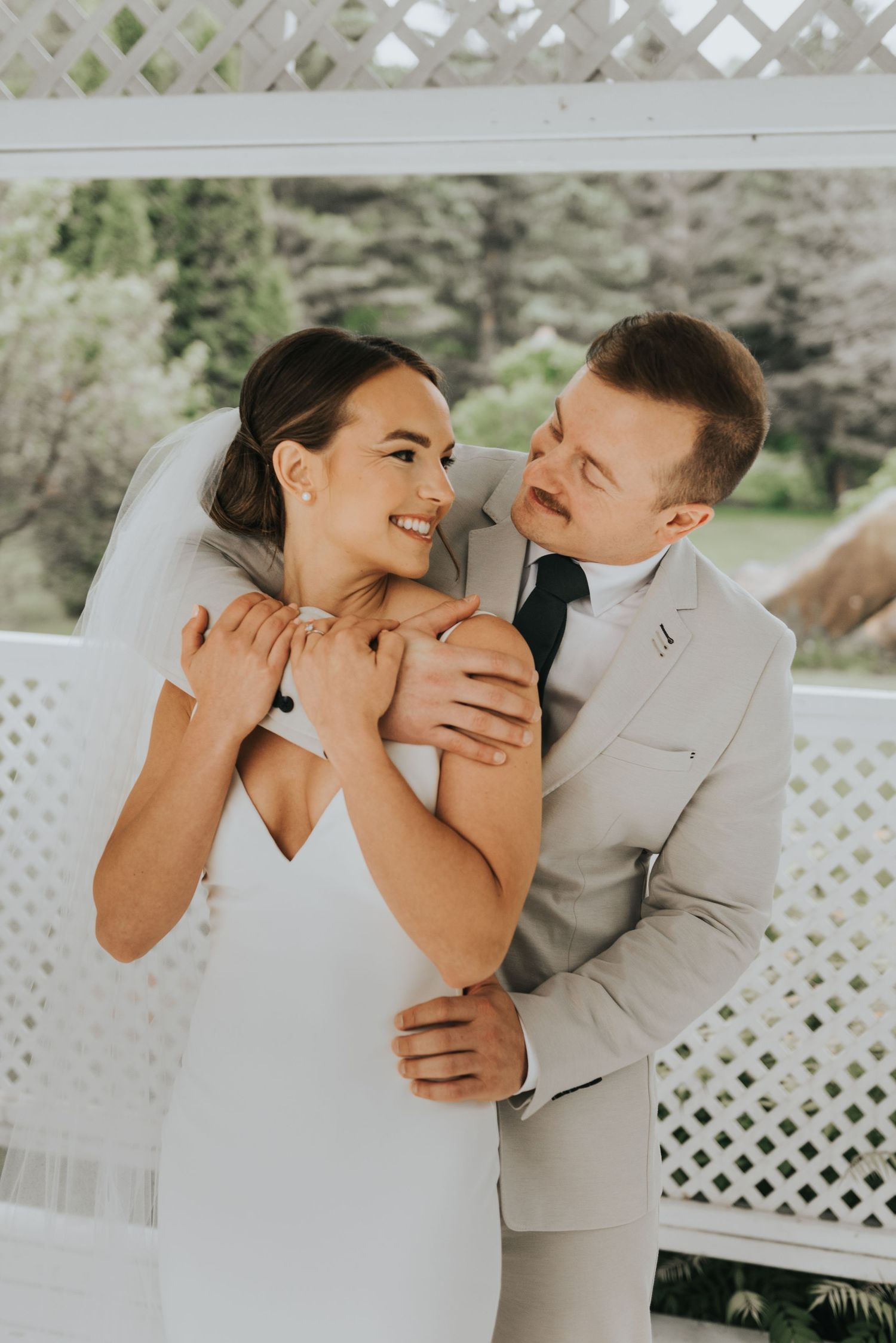 A couple in wedding attire share intimate moments in front of a white lattice backdrop during their wedding photoshoot.