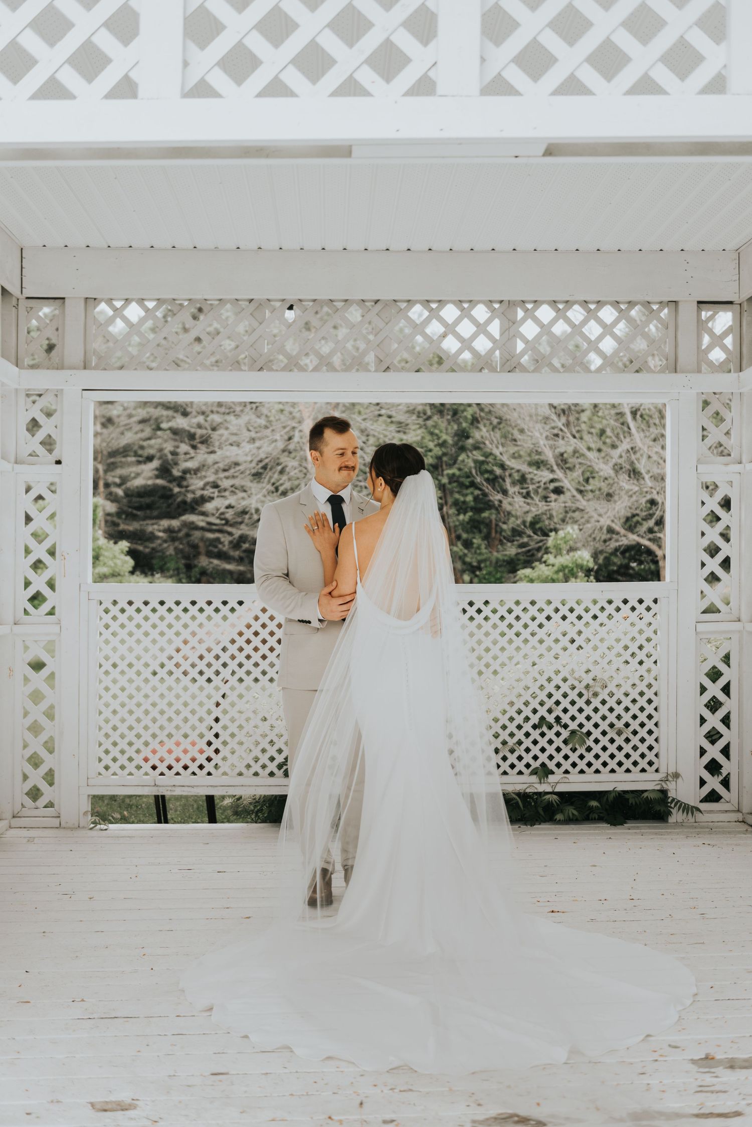 Newlywed couple sharing an intimate moment on a white lattice gazebo patio during their wedding celebration.