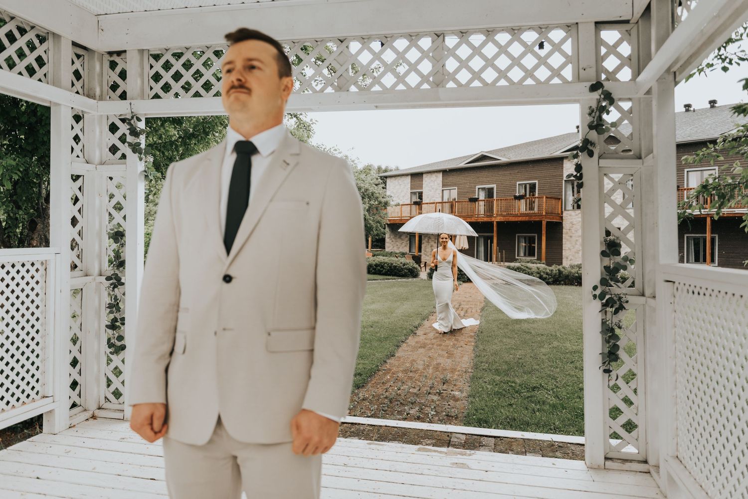 A first look moment captured at a white gazebo during a wedding ceremony with someone in a light beige suit.