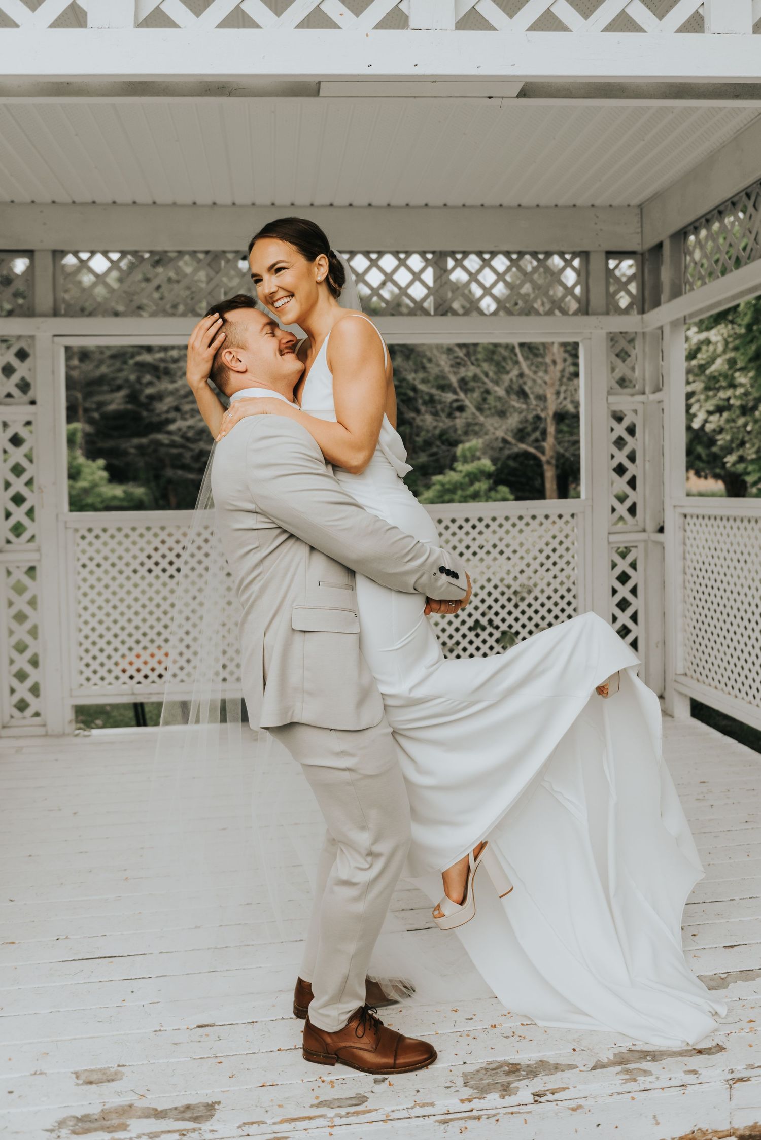 A couple in wedding attire shares a romantic dance on a white latticed porch during their special day.