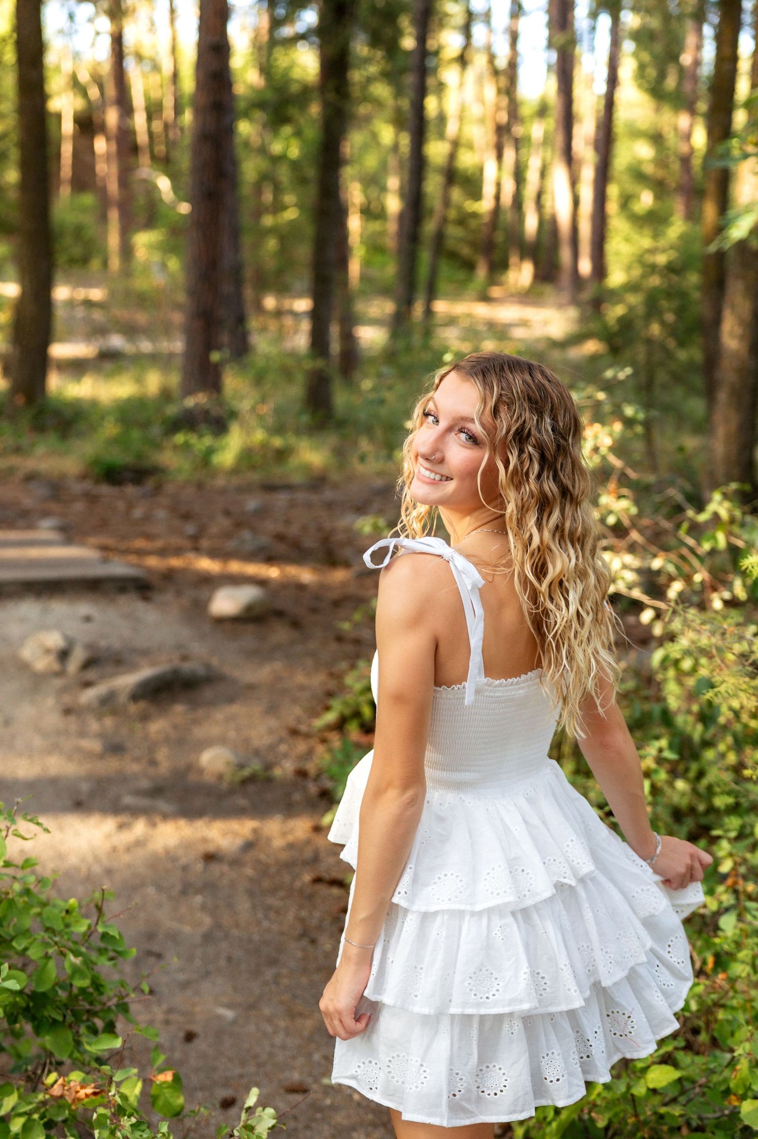 A white eyelet lace dress twirls in a sunlit forest setting creating a dreamy summer atmosphere.