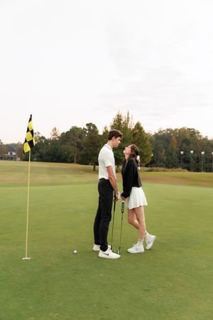 A couple shares a romantic moment on a scenic golf course with yellow flags visible in the background.