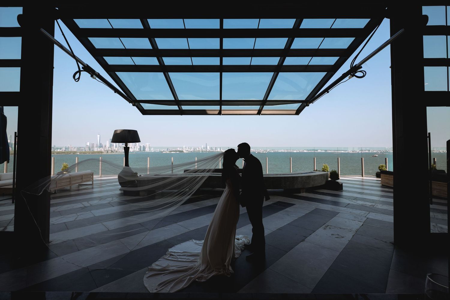 A silhouetted couple shares a romantic moment on a modern terrace overlooking a cityscape.