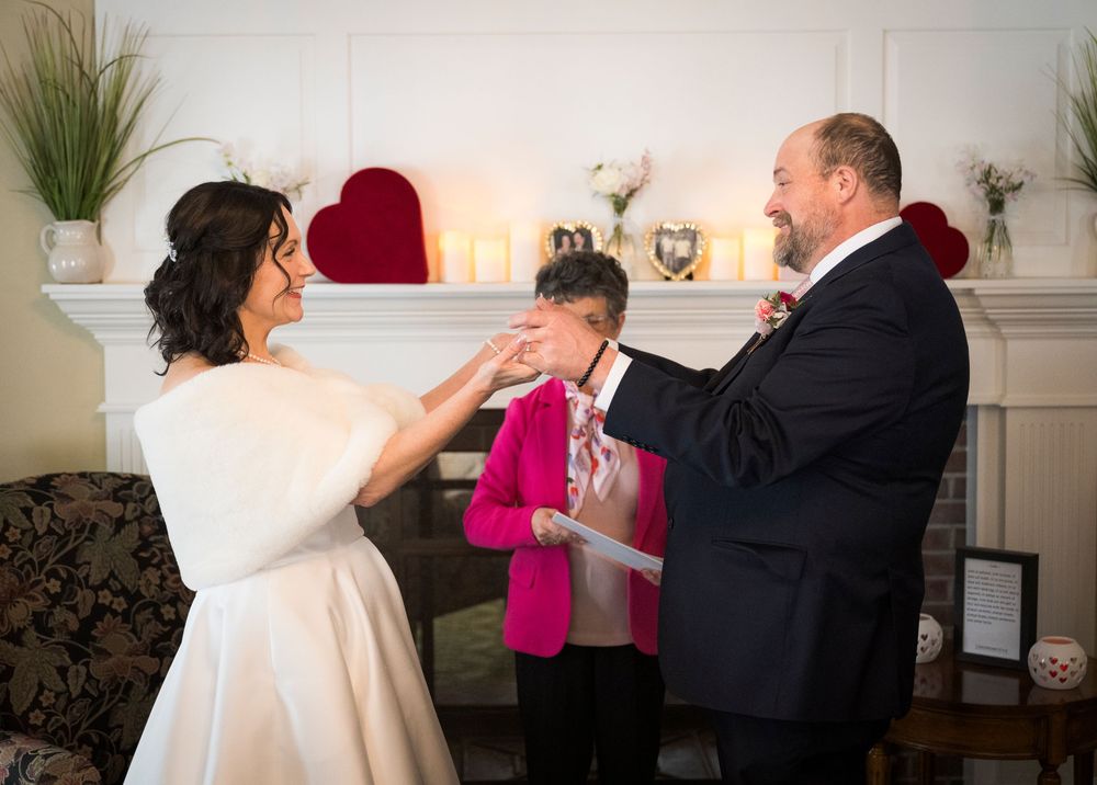 Couple exchanges vows during intimate indoor wedding ceremony with officiant in front of white fireplace mantel.