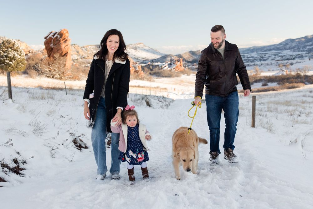 Family and dog walking together on a snowy path with scenic mountain views.