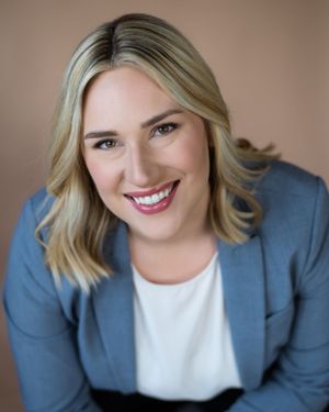 Professional headshot of person in blue blazer and white shirt smiling warmly against neutral background.