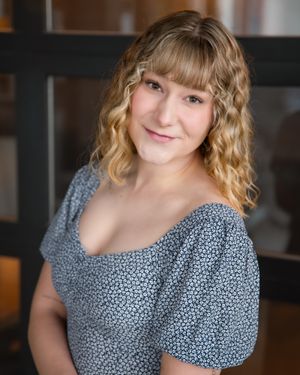 Professional portrait of someone wearing a blue floral dress with curled blonde hair.