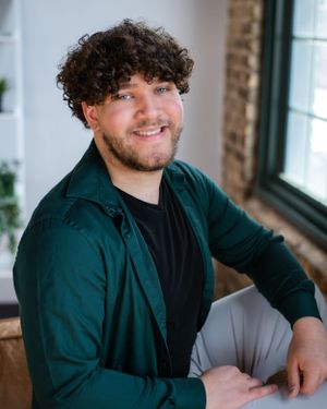 Professional portrait of person in dark green shirt with curly hair smiling at camera.