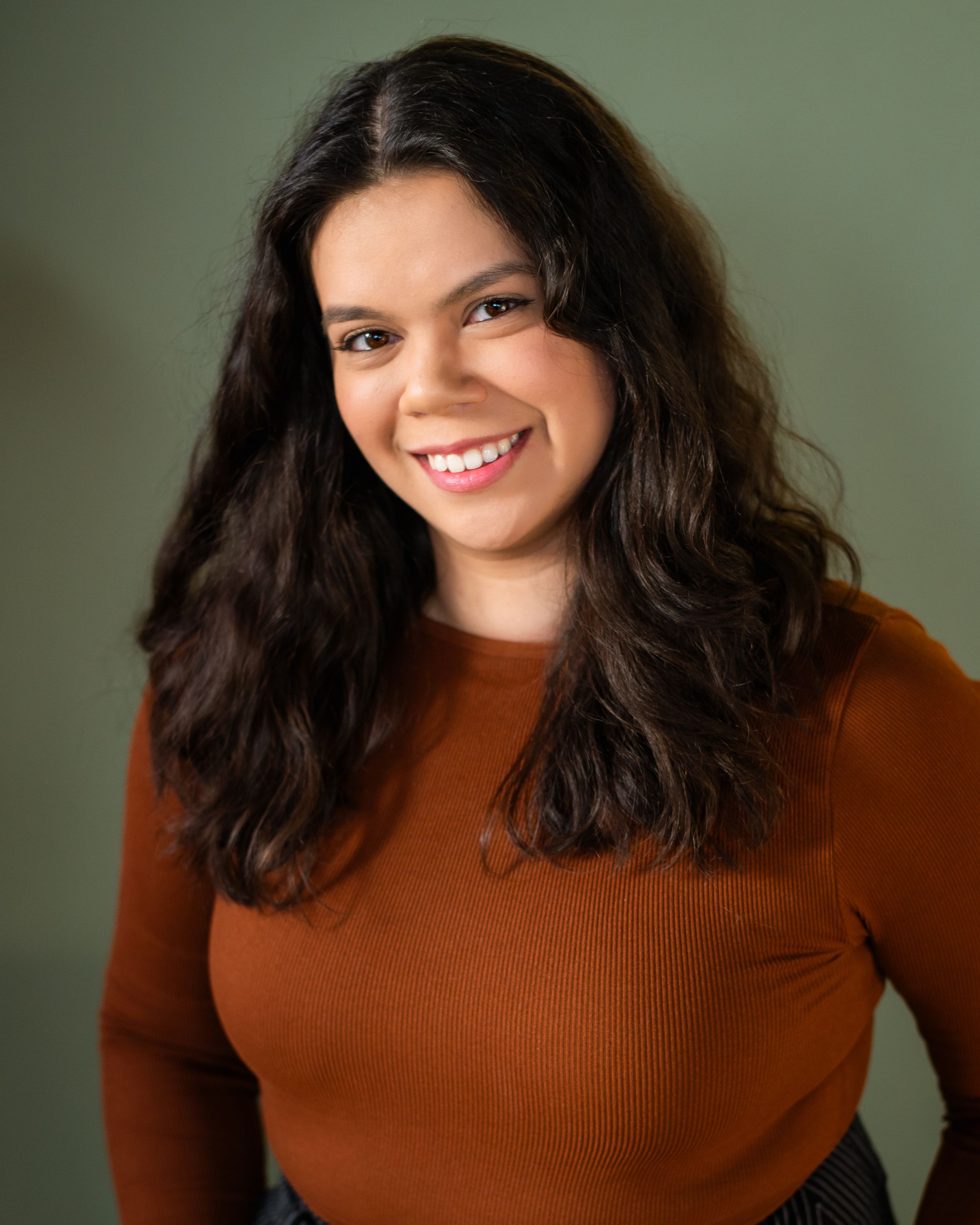 Portrait of a woman in a rust-colored ribbed sweater against a green background.
