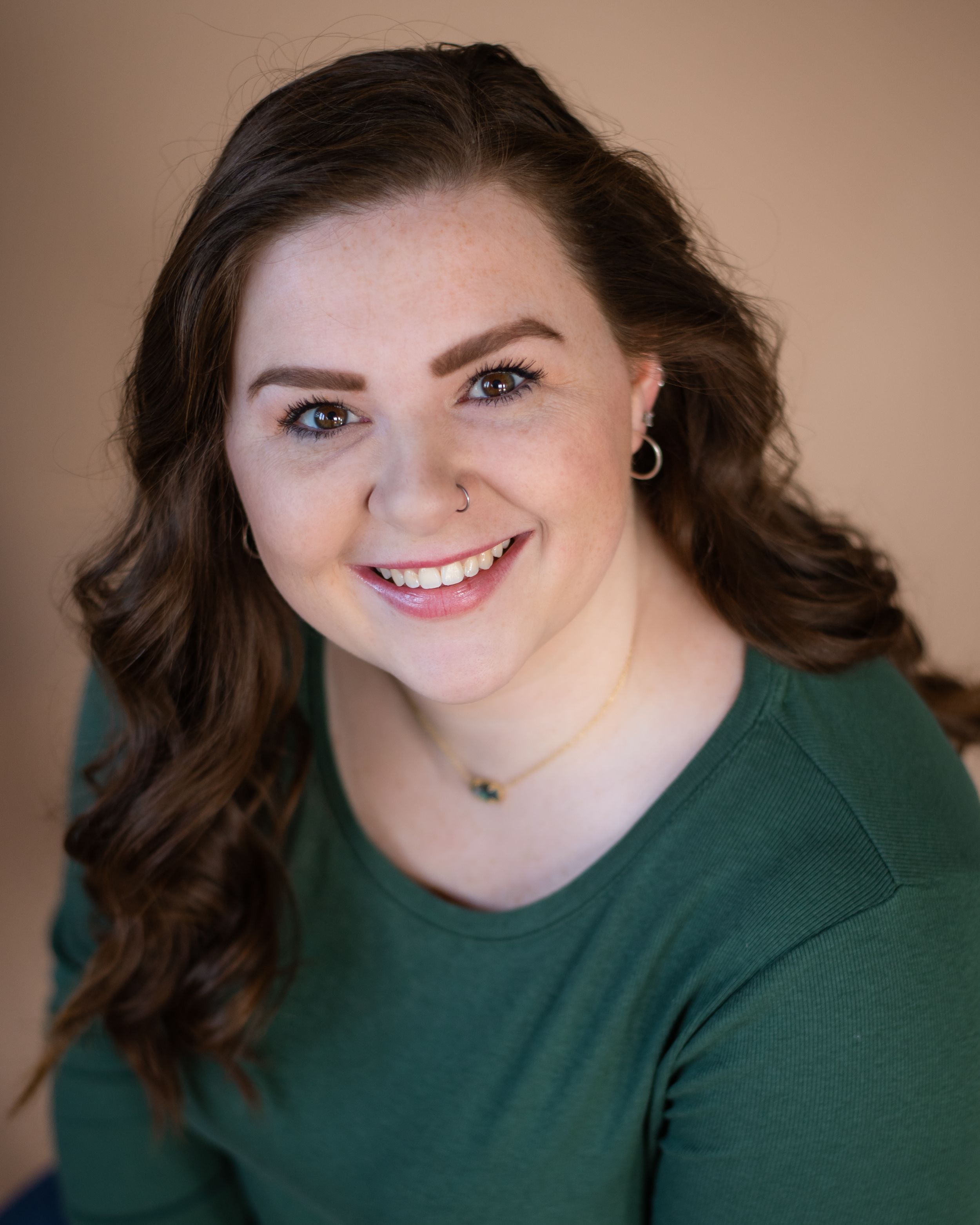 Studio portrait of person with long dark wavy hair wearing green top against warm background.