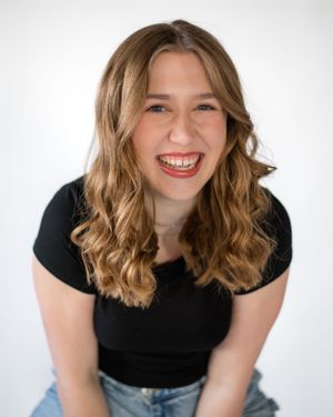 Portrait of person with wavy blonde hair wearing black top and jeans against white background.