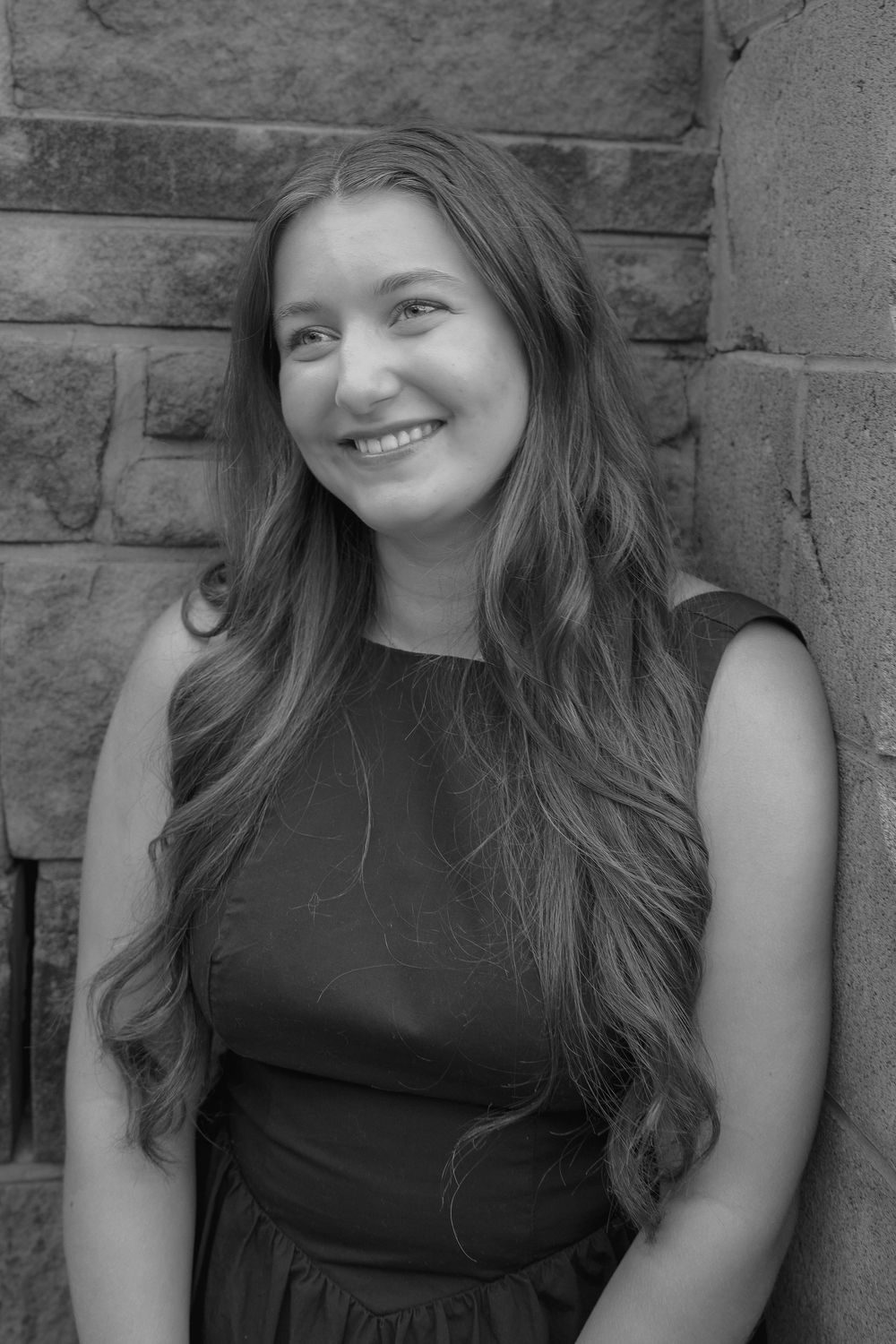 Black and white portrait series showing joyful expressions against a stone wall background.