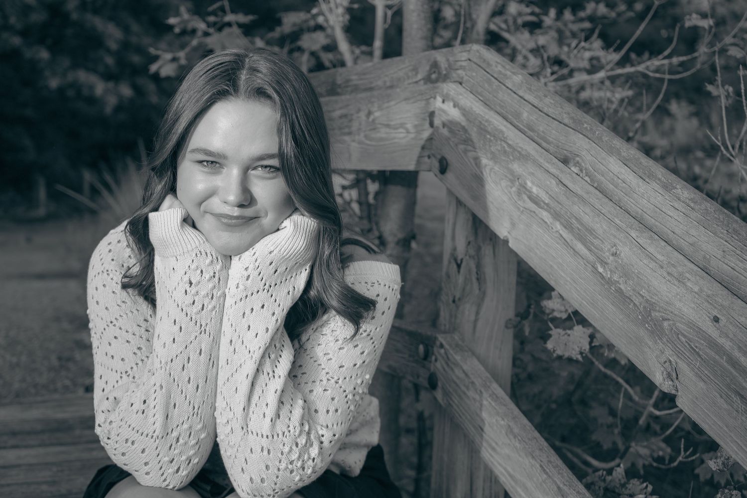 A person wearing a white knit sweater poses outdoors against a wooden fence in black and white.